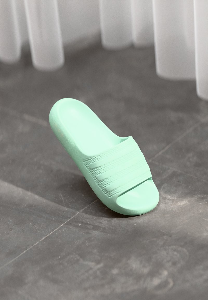 Mint green slide sandal made of textured plastic, featuring three horizontal stripes across the upper. Rounded toe and open back design.