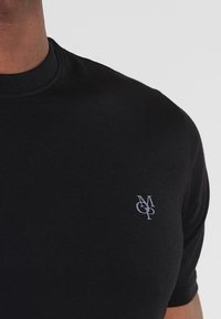 Schwarzes Kurzarm-T-Shirt aus Baumwolle mit Rundhalsausschnitt und einem kleinen grauen Logo auf der linken Brustseite. Glatte Textur.