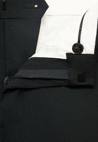 Pantalon noir avec une poche zippée, fermeture à bouton avec quincaillerie noire, et un revêtement en tissu blanc contrastant.