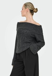 Sweter w kolorze ciemnoszarym z odsłoniętymi ramionami, w prążkowanym wzorze, z długimi rękawami i rozszerzanymi mankietami. W komplecie z czarnymi spodniami o wysokim stanie.