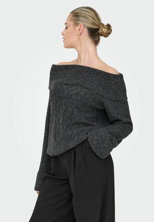 Pull-over gris foncé à épaules dénudées avec texture côtelée, manches longues et poignets évasés. Associé à un pantalon noir taille haute.