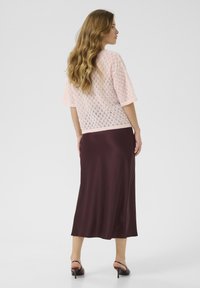 Haut court à manches courtes en tricot rose clair avec un motif en dentelle, associé à une jupe satin bourgogne foncé mi-longue, complétée par des sandales à talons.