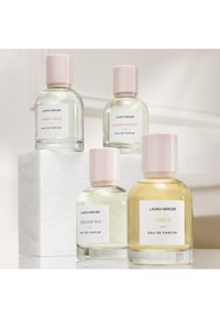 Fyra glasparfymflaskor med rosa lock, märkta "Ambre Vanille", "Almond Coconut", "Nérolis du Sud" och "Vanille", arrangerade på en vit pelare.