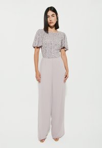 Jumpsuit lilla chiaro con top di paillettes e maniche a farfalla corte, design a gamba larga, realizzato in tessuto liscio e fluido.