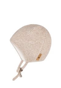 Beige knit baby hat with a soft lining, rounded top, and tie strings for secure fastening. Notable tag accent on the side.