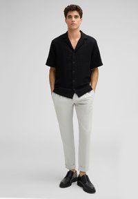 Schwarzes Kurzarmhemd mit strukturiertem Chevron-Muster, kombiniert mit hellgrauen Hosen und schwarzen Schnürschuhen.