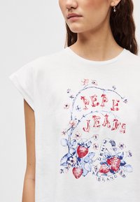 Λευκό βαμβακερό μπλουζάκι με σχέδιο από λουλούδια και φράουλες σε κόκκινο και μπλε. Κοντά μανίκια και στρογγυλή λαιμόκοψη.