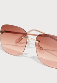 Ochelari de soare cu tentă roz, cu un design mare și pătrată, accente din metal de nuanță aurie și țevi nazale ajustabile. Temele transparente.