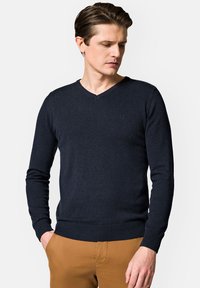 Granatowy sweter dziany z dekoltem w kształcie V, z prążkowanymi rękawami i dołem. Posiada subtelną logo na klatce piersiowej.