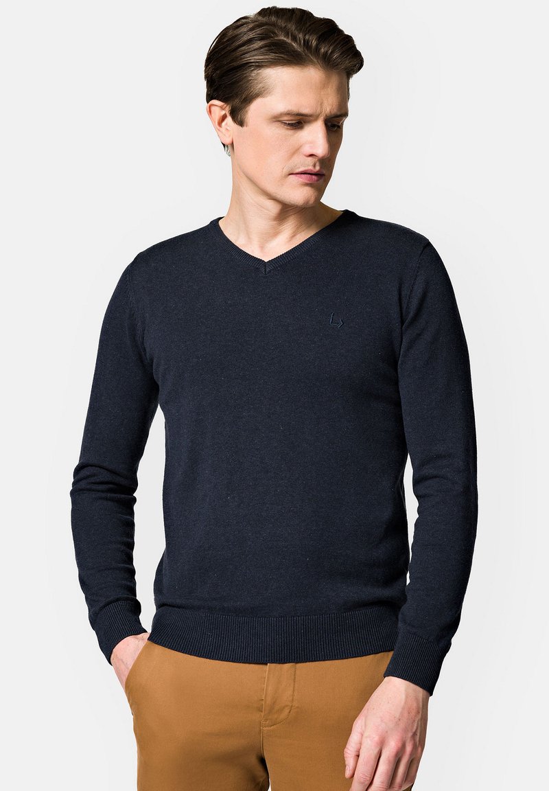 Granatowy sweter dziany z dekoltem w kształcie V, z prążkowanymi rękawami i dołem. Posiada subtelną logo na klatce piersiowej.