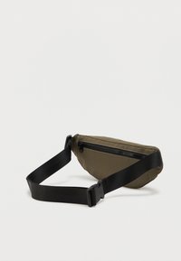 Khaki torba na pas z teksturowanym materiałem, czarnym zamkiem błyskawicznym i regulowanym czarnym paskiem. Delikatnie wygięty kształt dla idealnego dopasowania.