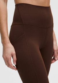 Kõrge vöökoht ja pruuni värvi legginsid, mis on valmistatud sujuvast ja venivast materjalist, külgõmbluste ja mugava, liibuva disainiga, mis tagab mugavuse ja liikumisvabaduse.