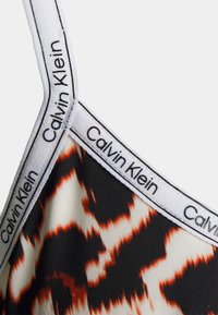 Bralette Calvin Klein com um padrão abstrato em preto, branco e laranja, apresentando uma marcação contrastante nas alças. Tecido suave e texturizado.