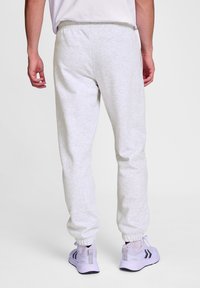 Helle graue Sweatpants aus weichem Material, mit einem elastischen Bund und Bündchen. Kombiniert mit lila Sportschuhen.