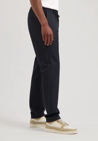 Navy tailored pants met een elastische tailleband, trekkoord, zijzakken en een gladde textuur. Gemaakt in combinatie met beige en witte sneakers.