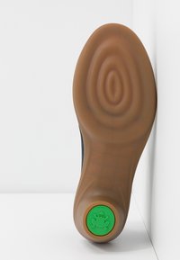 Semelle de chaussure avec une base en caoutchouc marron texturée et un logo circulaire vert avec une grenouille près du talon.