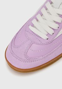 Light purple suede sneaker featuring white laces and a brown rubber sole. Concave stitch detailing and smooth leather accents are visible.