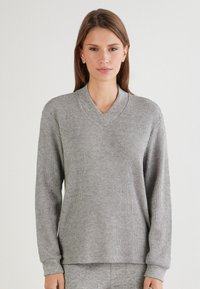 Grauer gerippter Strickpullover mit V-Ausschnitt, langen Ärmeln und Bündchen. Weiche Textur, lockerer Schnitt und dezentes Muster im gesamten Stoff.