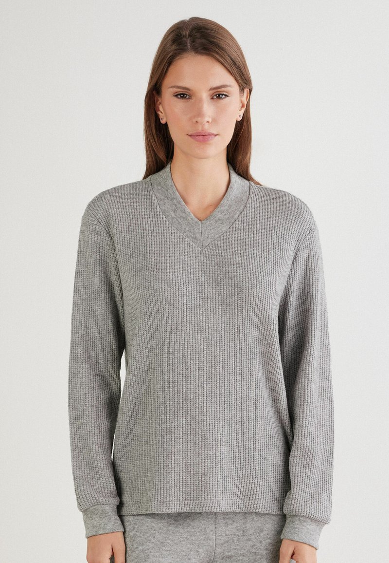 Grauer gerippter Strickpullover mit V-Ausschnitt, langen Ärmeln und Bündchen. Weiche Textur, lockerer Schnitt und dezentes Muster im gesamten Stoff.