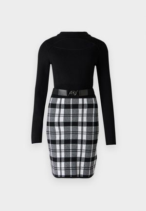 Top negro de manga larga ajustado combinado con una falda de cuadros en negro, blanco y gris de talle alto, ceñida con un cinturón negro con hebilla circular.