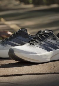 Chaussures de running Adidas noir et blanc avec semelles texturées reposant sur une surface en béton ensoleillée en extérieur.