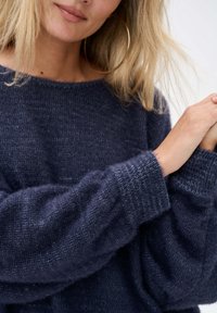 Granatowy sweter dzianinowy o luźnym kroju, z szerokimi prążkowanymi mankietami i teksturowanym wzorem, wykonany z miękkiego, puszystego materiału.