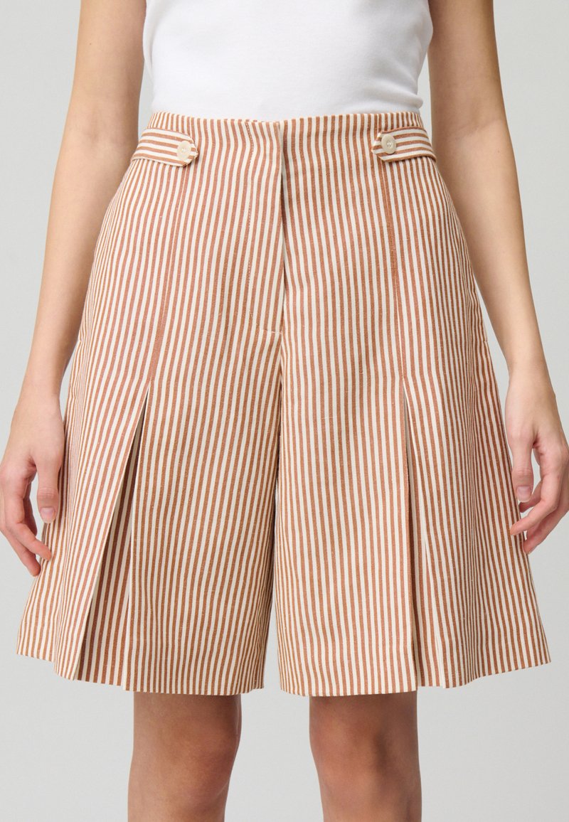 Pantalones cortos a rayas en beige y óxido con pliegues, que presentan dos botones frontales y bolsillos laterales, confeccionados en una tela texturizada.