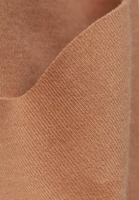 Textiel in een zachte, gestructureerde, gedempt oranje tint; kenmerkt zich door een fijn gebreid patroon met een licht matte afwerking. De randen zijn subtiel omgevouwen.