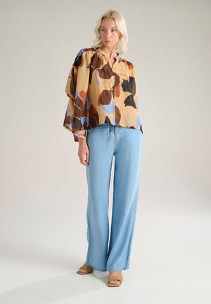 Blusa semitrasparente multicolore con vestibilità ampia e chiusura frontale a bottoni. Abbinata a jeans a gamba larga blu chiaro con vita alta e sandali beige.