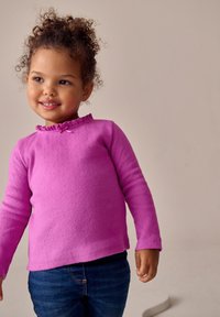 Top rosa de manga larga con un escote fruncido y pequeño detalle de lazo. Textura suave y ajuste relajado, combinado con vaqueros azules.