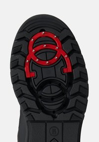 Podešev černé gumové boty s hlubokým vzorem běhounu, obsahující červený kruhový motiv a kovové hroty pro lepší přilnavost a trakci.