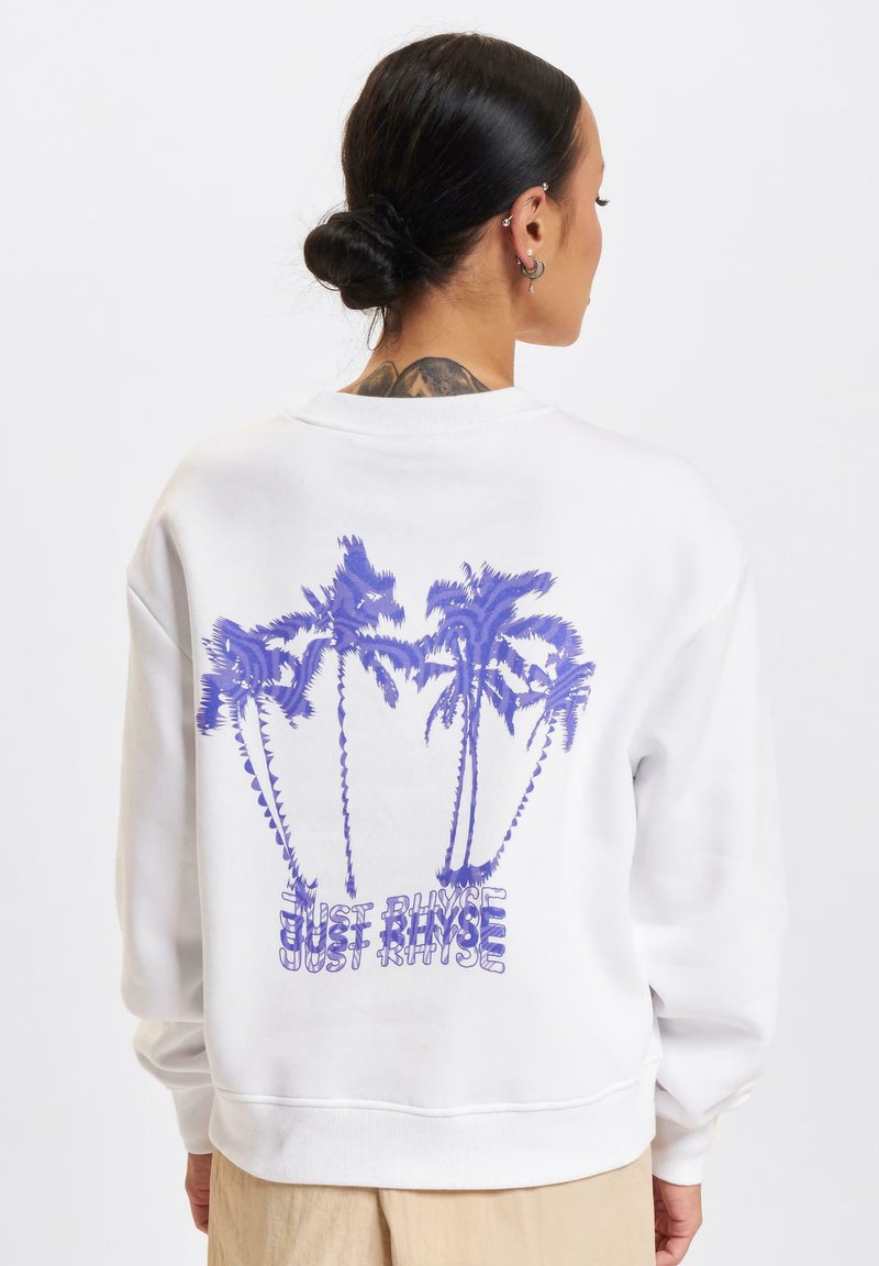 Weißes Sweatshirt mit lila Palmen-Motiv und dem Text "JUST RINSE" auf dem Rücken. Verfügt über gerippte Bündchen und Saum sowie eine weiche Stofftextur.