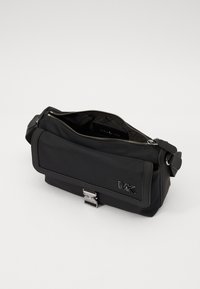 Borsa a tracolla nera in nylon con hardware argentato, chiusura con zip, e patta frontale con logo impresso. Finitura testurizzata, tracolla regolabile.