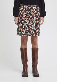 Jupe noire avec un motif abstrait multicolore, présentant une coupe légèrement évasée. Associée à des bottes en cuir marron hautes.
