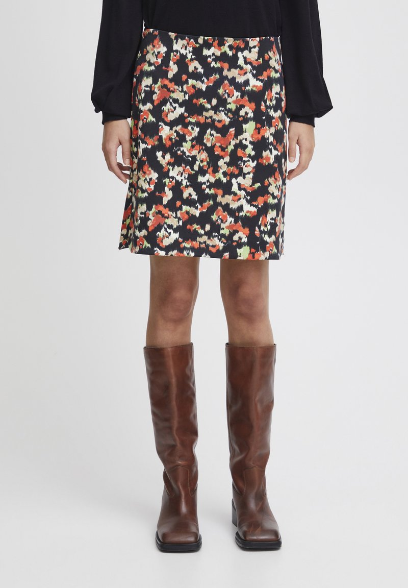Jupe noire avec un motif abstrait multicolore, présentant une coupe légèrement évasée. Associée à des bottes en cuir marron hautes.