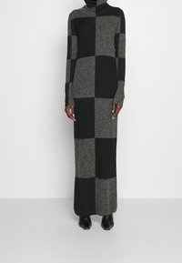 Lång, åtsittande klänning i grått och svart rutmönster. Har en hög polokrage och långa ärmar. Tillverkad av ett mjukt, texturerat stickat material.