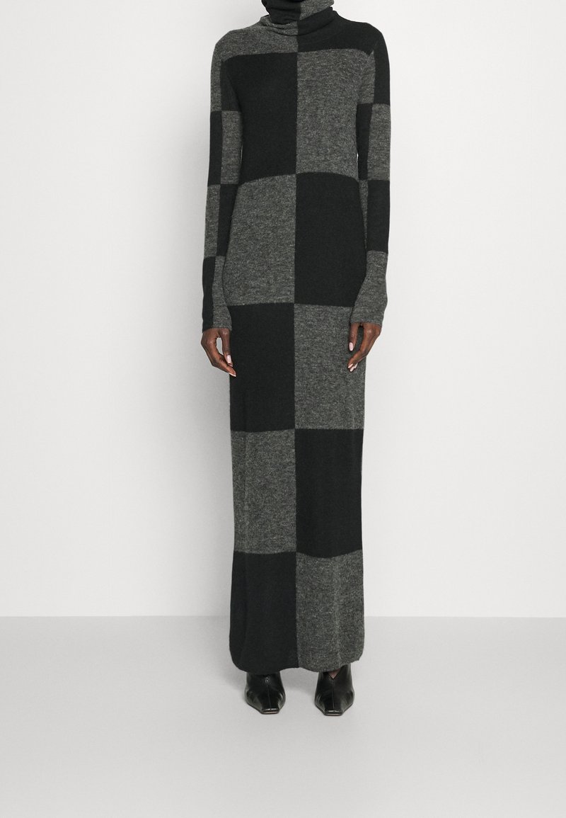 Lång, åtsittande klänning i grått och svart rutmönster. Har en hög polokrage och långa ärmar. Tillverkad av ett mjukt, texturerat stickat material.