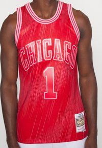 Punainen koripallopaita, jossa on valkoiset kirjaimet "CHICAGO" ja numero "1". Raidallinen kaula-aukko, teksturoidut kuviot ja ommeltu etiketti.