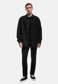 Camisa de mezclilla negra con botones, combinada con una camiseta negra y jeans ajustados negros. Zapatillas negras con cordones blancos, de diseño minimalista.