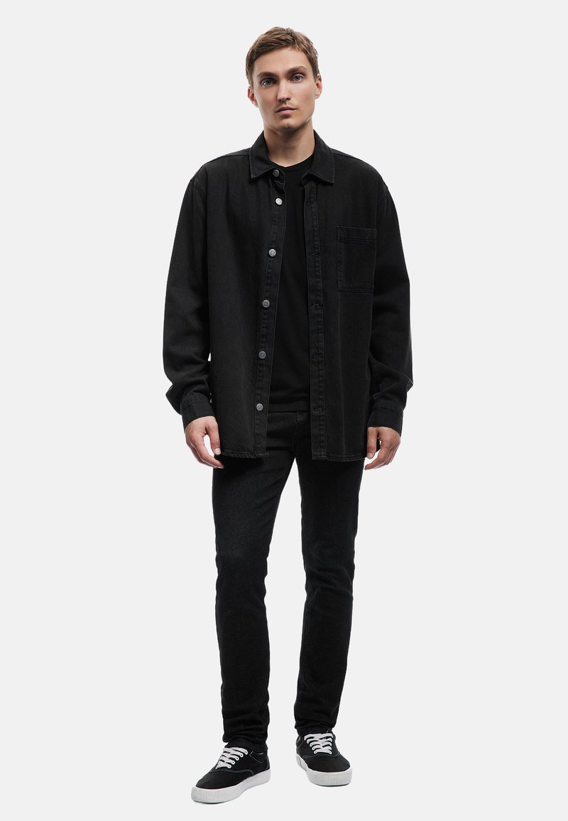 Camisa de mezclilla negra con botones, combinada con una camiseta negra y jeans ajustados negros. Zapatillas negras con cordones blancos, de diseño minimalista.