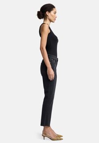 Schwarzes rippiges Tanktop, kombiniert mit hoch taillierten, geraden schwarzen Jeans. Gelbe Slingback-Pumps mit Schlangenprint vervollständigen das Outfit.