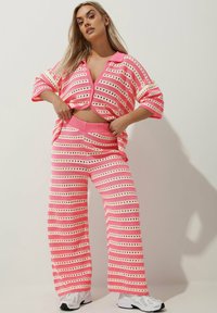 Set di abbigliamento da casa lavorato a maglia in rosa e panna con ampie strisce e ritagli circolari. Presenta un top corto con colletto e pantaloni a gamba larga.