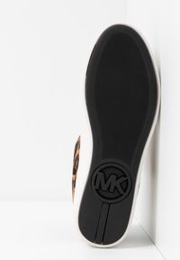 Semelle en caoutchouc d'une basket avec une adhérence texturée et le logo MK, côté montrant une tige en tissu imprimé léopard.