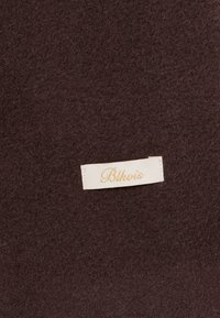 Dark brown felt material features a small cream tag labeled "Blkvis" in gold lettering, indicating brand details. Textured surface visible.