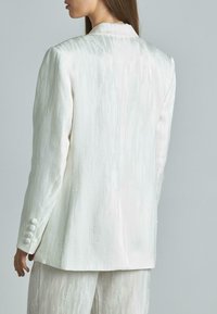 Witte blazer met een gestructureerde afwerking, enkelvoudig aangekleed ontwerp en een vierknops sluiting op de manchetten. Glad materiaal met subtiele glans.