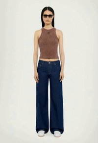 Pruun lühike top ümmarguse kaelusega ja brodeeritud detailidega, kombineeritud laia säärega tumehallide teksade ning valgete slip-on kingadega.