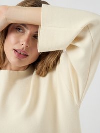 Maglione a maglia beige chiaro con una vestibilità ampia, maniche larghe e scollo rotondo; morbida texture e design minimale senza motivi o dettagli.