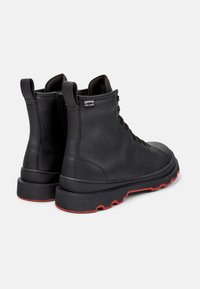 Black leather boots with a rugged design and red soles, featuring a lace-up front and a zip closure at the back.