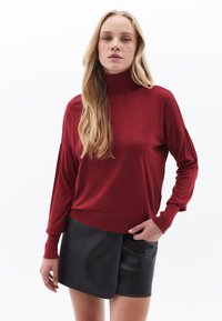 Maglione a collo alto color cremisi in morbido tessuto, con maniche lunghe e vestibilità rilassata, abbinato a una gonna nera in ecopelle.