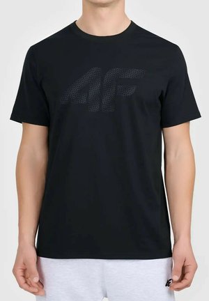 Mężczyzna ubrany w czarną koszulkę z krótkim rękawem z teksturowanym logo "4F" oraz jasnoszare szorty z małym logo "4F" na nodze.